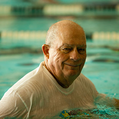 A man smiles as he walks laps in the pool. Links to Over Age 70